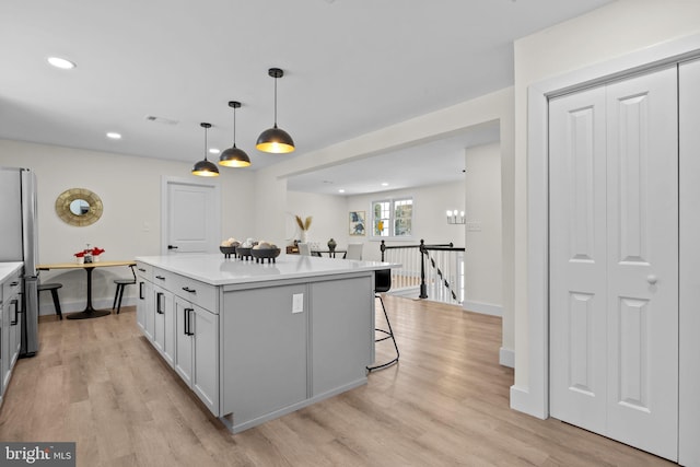 kitchen featuring stainless steel refrigerator, gray cabinetry, a center island, hanging light fixtures, and a kitchen breakfast bar