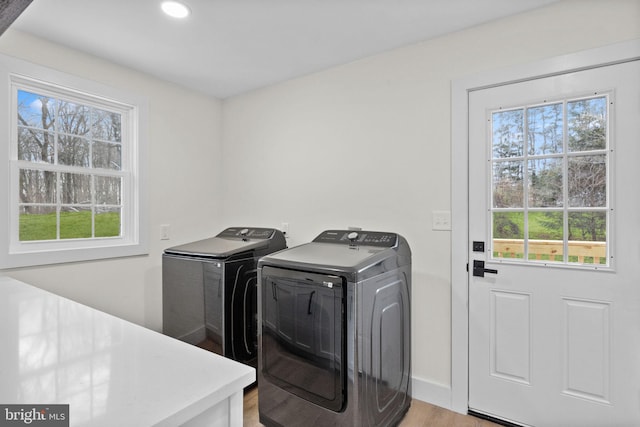 clothes washing area with washing machine and clothes dryer and light hardwood / wood-style flooring