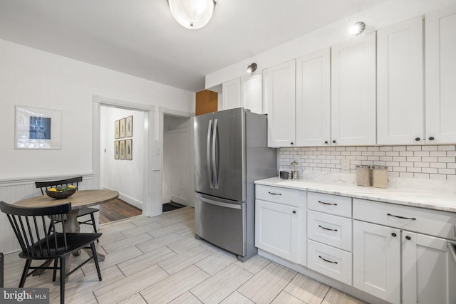 kitchen with light stone counters, white cabinetry, decorative backsplash, and stainless steel refrigerator