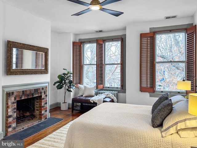 bedroom with ceiling fan, dark hardwood / wood-style flooring, and a brick fireplace