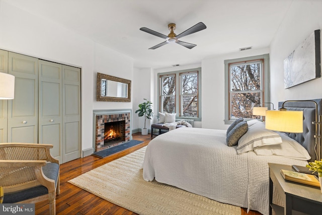 bedroom with a closet, ceiling fan, a brick fireplace, and dark hardwood / wood-style flooring