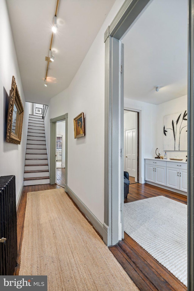 corridor featuring rail lighting, hardwood / wood-style floors, and radiator