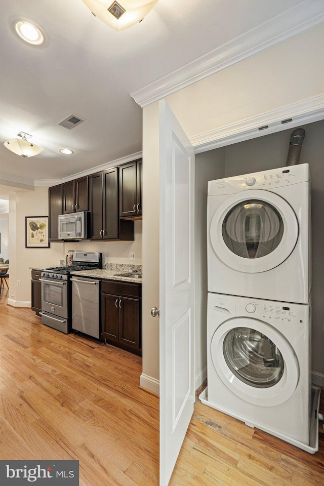 clothes washing area with stacked washer / drying machine, crown molding, and light hardwood / wood-style flooring