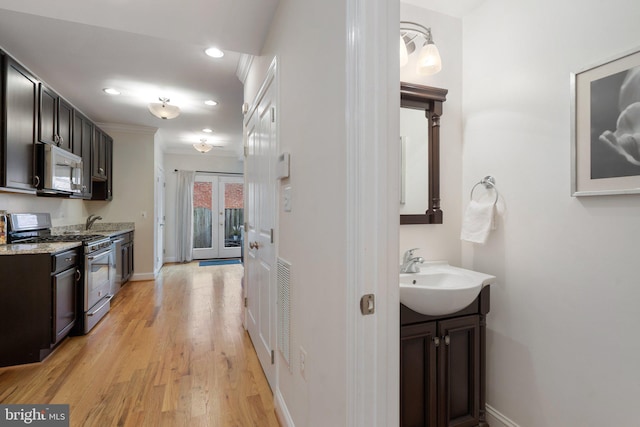 interior space with dark brown cabinetry, sink, light hardwood / wood-style flooring, appliances with stainless steel finishes, and light stone countertops