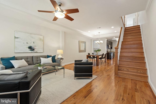 living room with hardwood / wood-style flooring, ornamental molding, and ceiling fan with notable chandelier