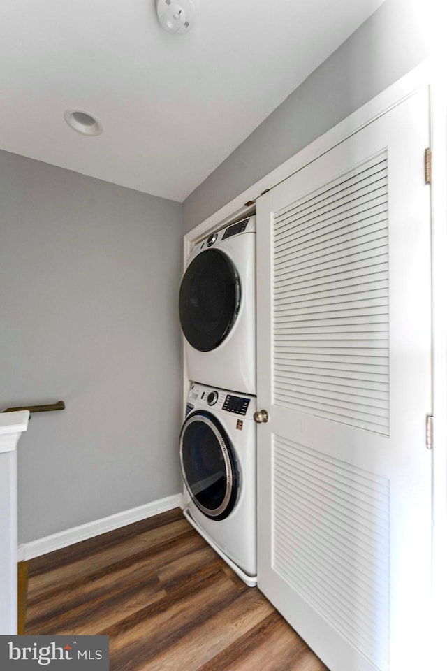 laundry room featuring stacked washer / dryer and dark wood-type flooring