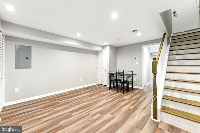 basement featuring electric panel and light hardwood / wood-style flooring