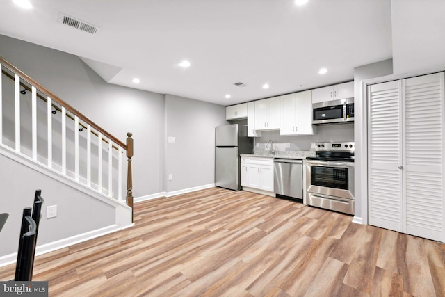 kitchen featuring white cabinets, sink, light stone countertops, light wood-type flooring, and appliances with stainless steel finishes