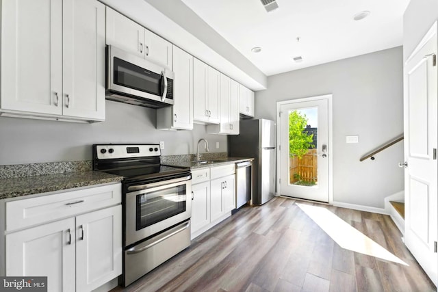 kitchen with dark stone countertops, hardwood / wood-style floors, white cabinets, and appliances with stainless steel finishes