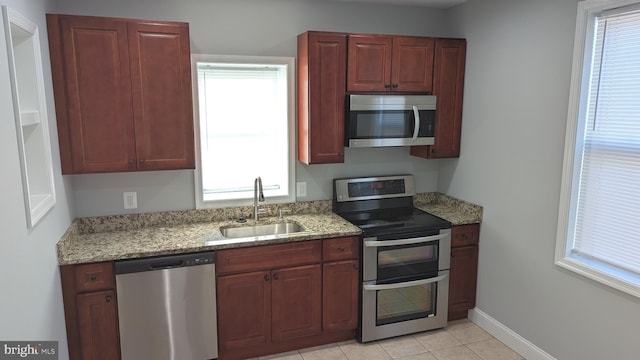 kitchen with appliances with stainless steel finishes, plenty of natural light, light stone counters, and sink