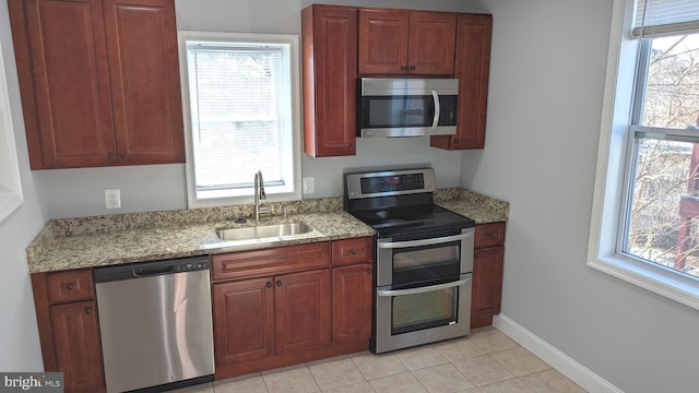 kitchen with appliances with stainless steel finishes, a healthy amount of sunlight, light stone counters, and sink