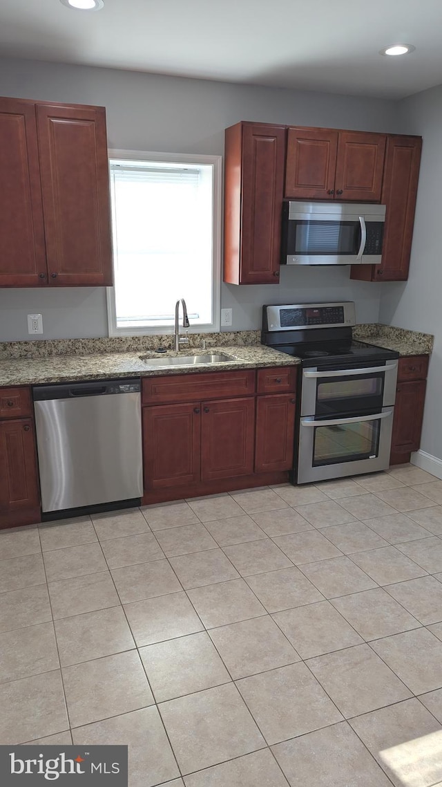 kitchen featuring light tile patterned floors, appliances with stainless steel finishes, light stone counters, and sink