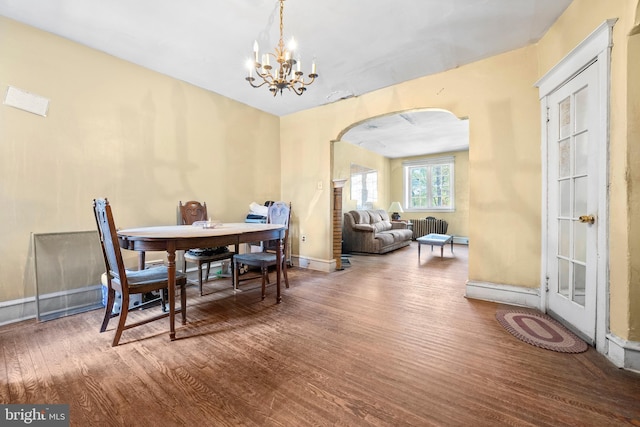 dining area with radiator, hardwood / wood-style floors, and an inviting chandelier