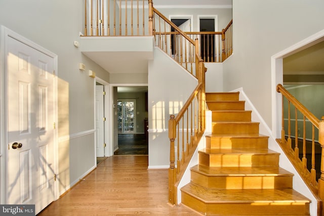 staircase with hardwood / wood-style flooring, a high ceiling, and ornamental molding