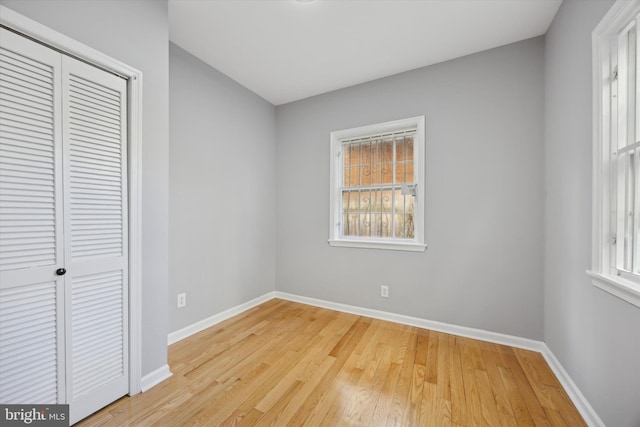 unfurnished bedroom featuring light wood-type flooring, a closet, and multiple windows