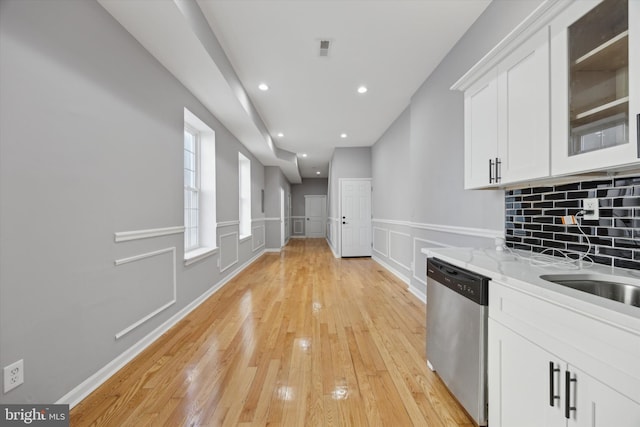 kitchen with light stone countertops, dishwasher, light hardwood / wood-style floors, tasteful backsplash, and white cabinets