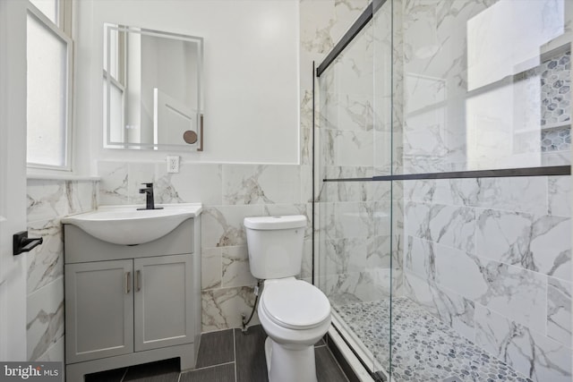 bathroom featuring toilet, vanity, tile walls, and a shower with shower door