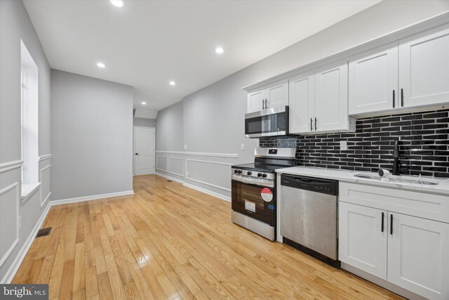 kitchen featuring stainless steel appliances, sink, white cabinets, light wood-type flooring, and backsplash