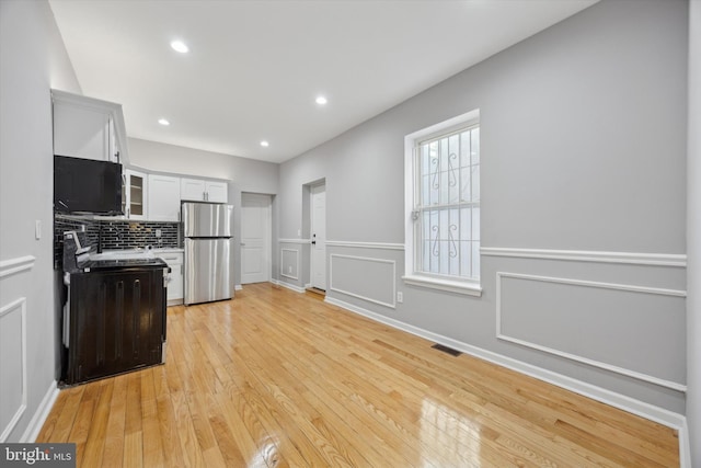 kitchen with white cabinets, decorative backsplash, stainless steel refrigerator, and light hardwood / wood-style flooring