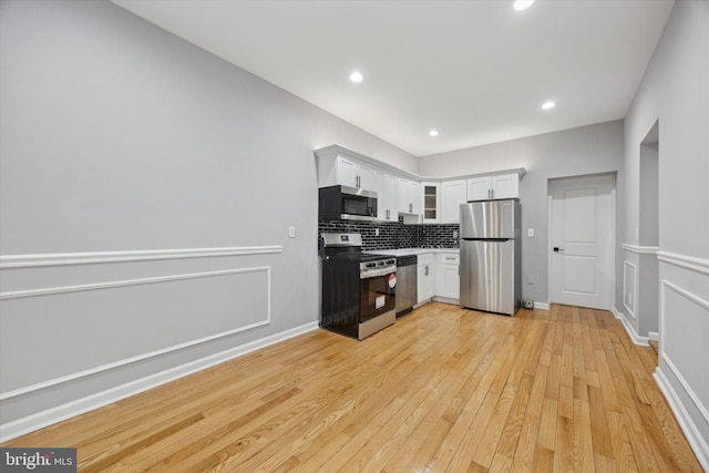 kitchen with appliances with stainless steel finishes, light hardwood / wood-style floors, white cabinets, and backsplash