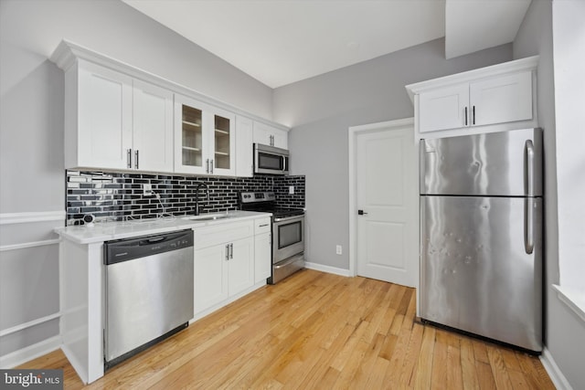 kitchen with stainless steel appliances, light wood-type flooring, backsplash, white cabinets, and sink