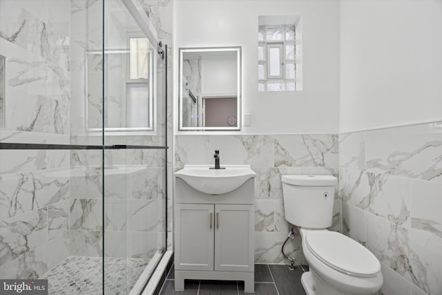 bathroom with toilet, a tile shower, vanity, and tile walls