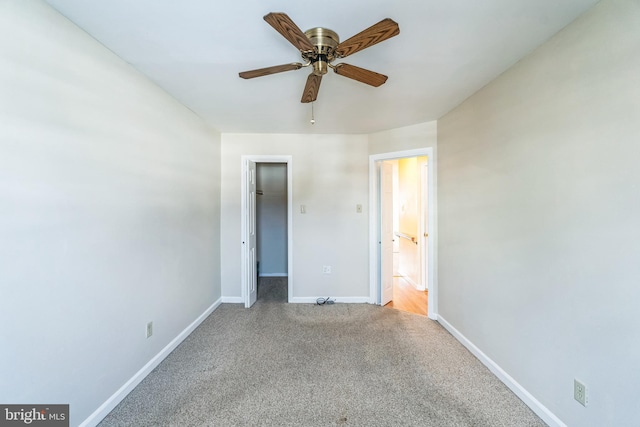 unfurnished bedroom featuring light carpet, a walk in closet, a closet, and ceiling fan