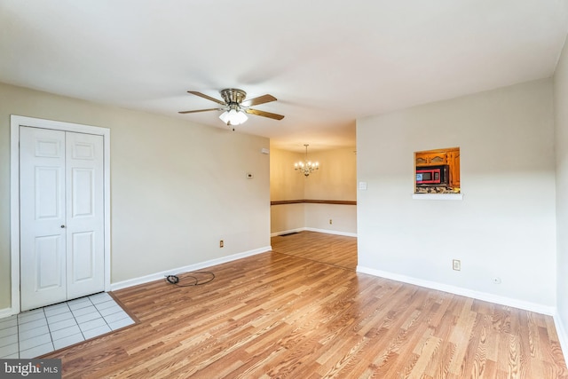 empty room with light hardwood / wood-style flooring and ceiling fan with notable chandelier