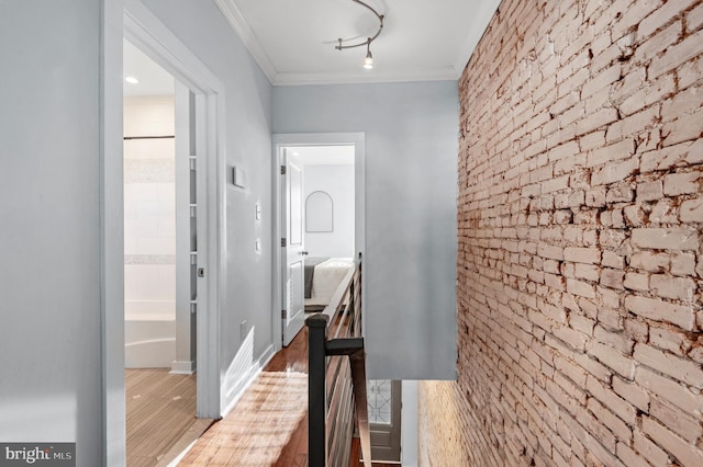 corridor with wood-type flooring, ornamental molding, and brick wall