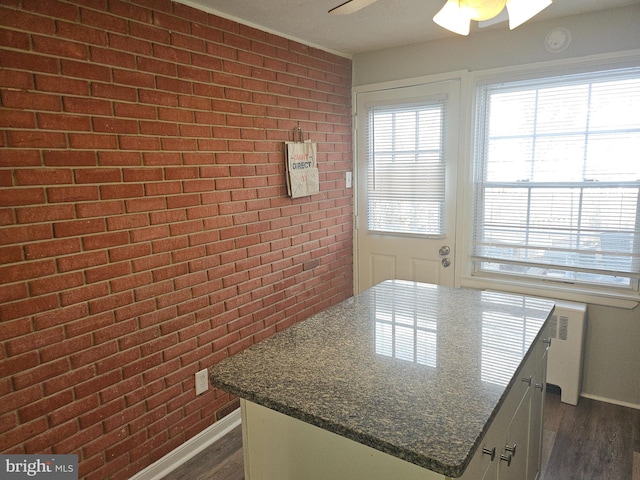 kitchen featuring dark stone countertops, dark hardwood / wood-style flooring, radiator, a kitchen island, and ceiling fan