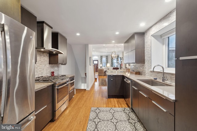 kitchen featuring sink, wall chimney range hood, tasteful backsplash, pendant lighting, and appliances with stainless steel finishes