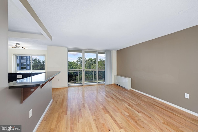 unfurnished living room featuring floor to ceiling windows, light hardwood / wood-style flooring, a textured ceiling, and radiator heating unit