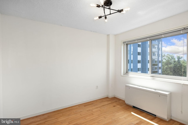 spare room featuring radiator heating unit, a chandelier, a textured ceiling, and light hardwood / wood-style floors