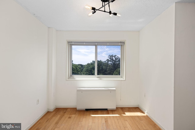 spare room featuring a textured ceiling, light hardwood / wood-style floors, and a notable chandelier