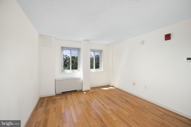 unfurnished room featuring radiator heating unit, a textured ceiling, and light hardwood / wood-style flooring