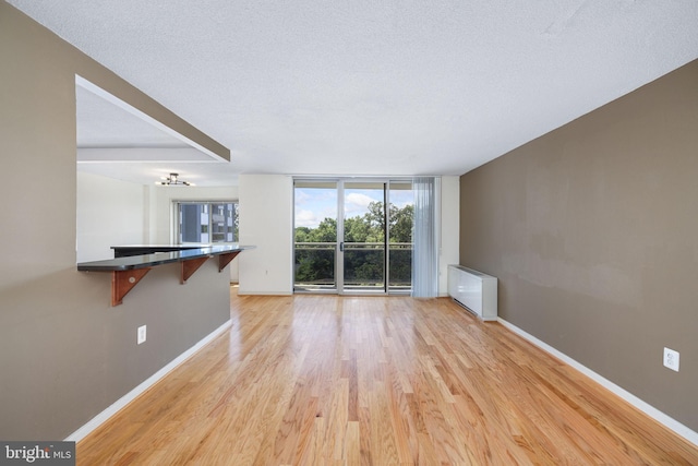 unfurnished living room with a textured ceiling, expansive windows, radiator, and light hardwood / wood-style floors