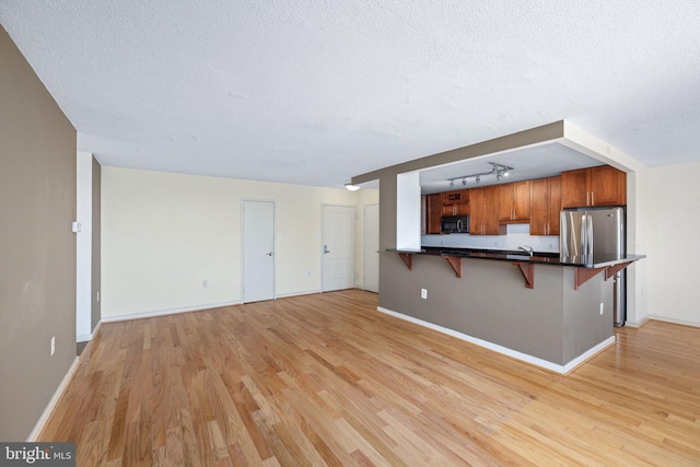 unfurnished living room with rail lighting, sink, light wood-type flooring, and a textured ceiling