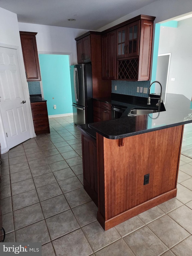 kitchen featuring a peninsula, a sink, freestanding refrigerator, dark countertops, and glass insert cabinets