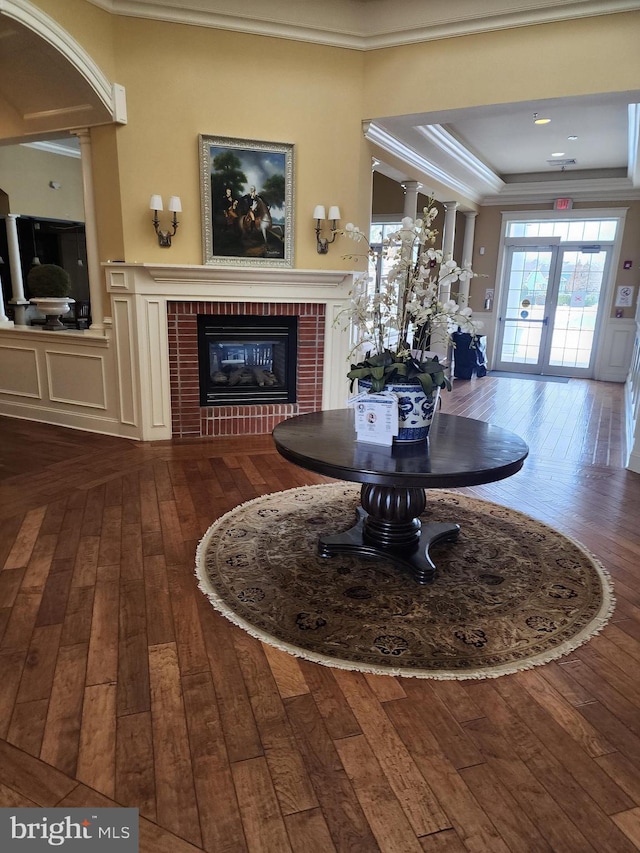 unfurnished dining area featuring french doors, a fireplace, a raised ceiling, dark wood-type flooring, and ornamental molding