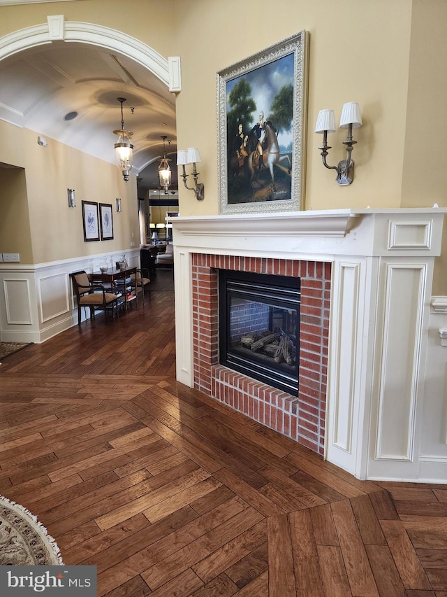 living area with arched walkways, wainscoting, a brick fireplace, and dark wood finished floors