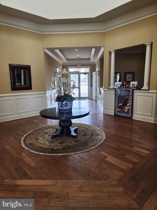 foyer with ornate columns, dark wood-style floors, a decorative wall, and crown molding