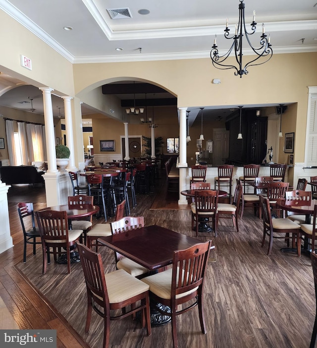 dining space featuring a chandelier, dark wood-style flooring, visible vents, ornamental molding, and decorative columns