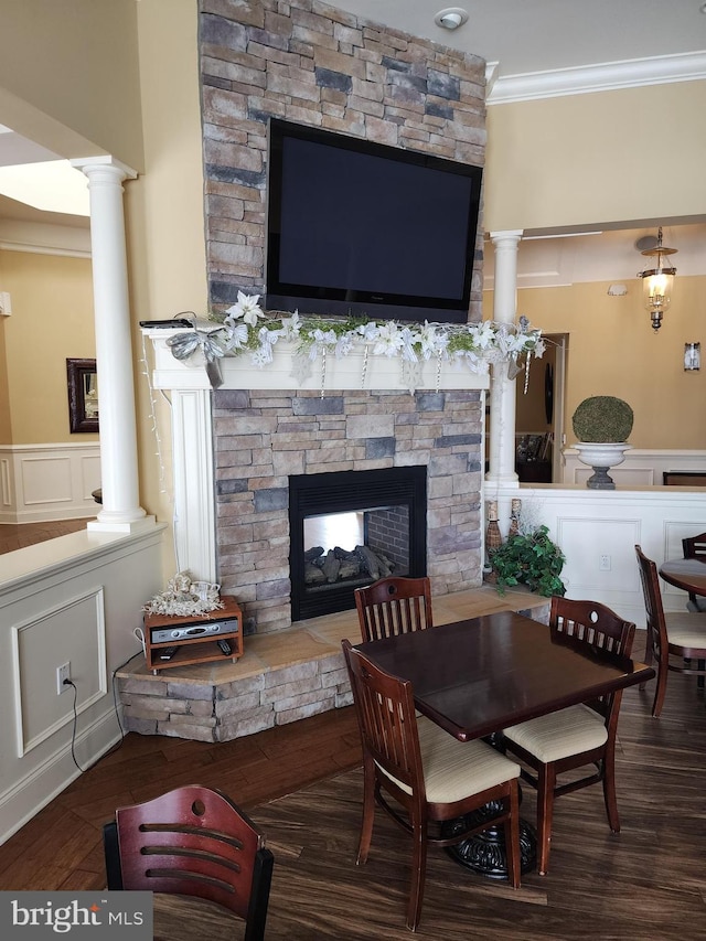 dining room featuring ornamental molding, a stone fireplace, and ornate columns