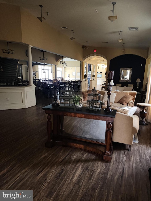 living area with arched walkways, dark wood finished floors, and visible vents