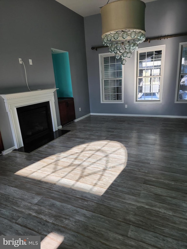 unfurnished living room featuring baseboards, a fireplace with flush hearth, dark wood finished floors, and an inviting chandelier