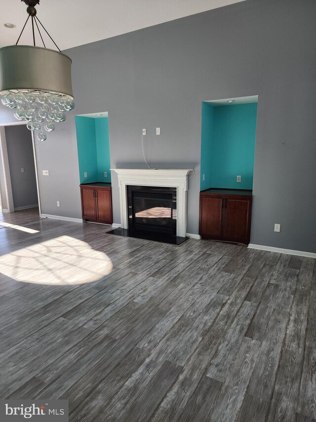 unfurnished living room featuring a glass covered fireplace, dark wood-style flooring, baseboards, and an inviting chandelier