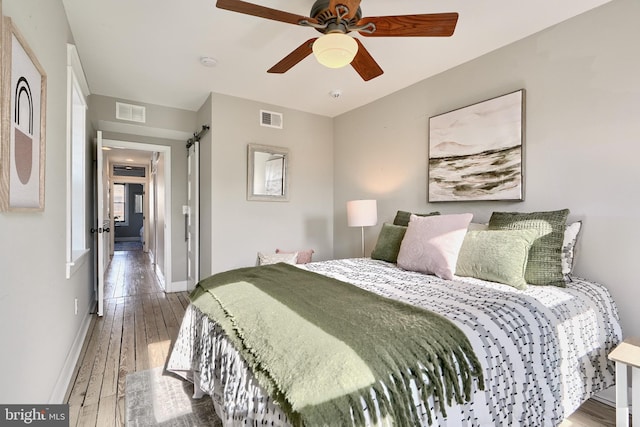 bedroom featuring wood-type flooring, a barn door, and ceiling fan