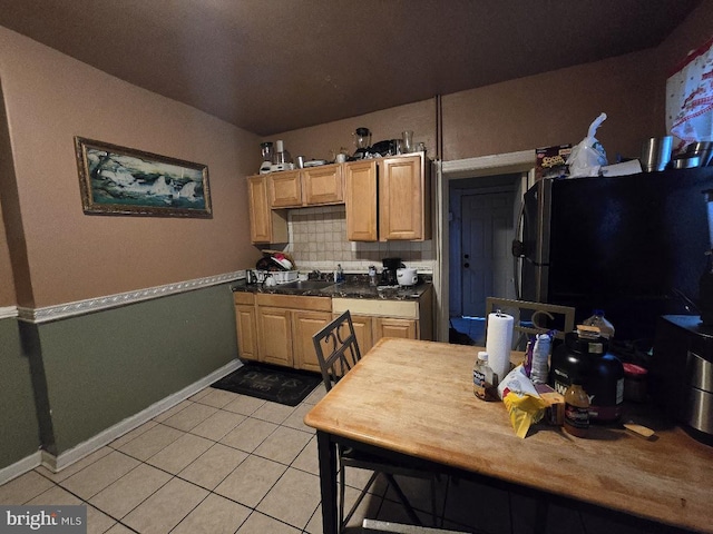 kitchen with decorative backsplash, black fridge, light tile patterned floors, and light brown cabinetry