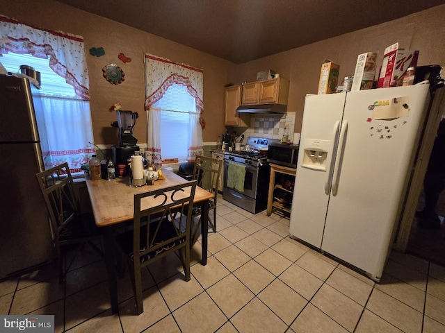 kitchen featuring white refrigerator with ice dispenser, refrigerator, decorative backsplash, light tile patterned flooring, and stainless steel range with gas stovetop