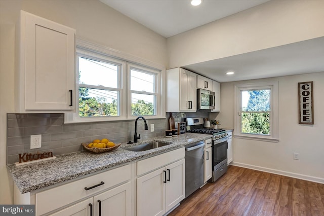 kitchen featuring stainless steel appliances, sink, white cabinetry, light stone counters, and wood-type flooring